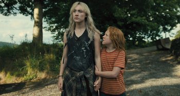 Movie still from “How I Live Now” (2013), directed by Kevin Macdonald – Two young people standing next to each other on a dirt road; Medium shot, Over the shoulder angle