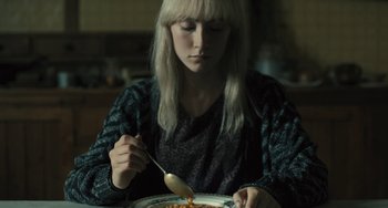 Movie still from “How I Live Now” (2013), directed by Kevin Macdonald – A woman sitting at a table with a plate of food; Close Up shot, High angle