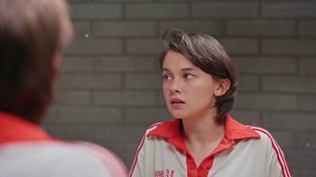 Movie still from “How It Ends” (2021), directed by Daryl Wein – A young boy in a red and white shirt looks to his left; Close Up shot, Over the shoulder angle