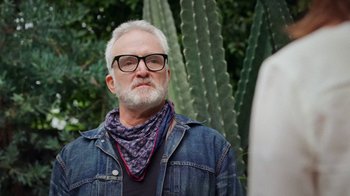 Movie still from “How It Ends” (2021), directed by Daryl Wein – An older man with a beard wearing glasses and a denim jacket; Close Up shot, Low angle