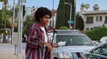 Movie still from “How It Ends” (2021), directed by Daryl Wein – A person standing on the side of the road holding a microphone; Medium shot, Low angle