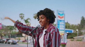 Movie still from “How It Ends” (2021), directed by Daryl Wein – A young man standing at a microphone in front of a palm tree; Medium shot, Low angle