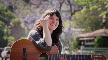 Movie still from “How It Ends” (2021), directed by Daryl Wein – A woman holding a guitar and smiling for the camera; Close Up shot, Low angle