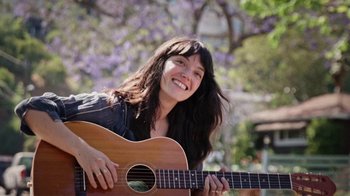 Movie still from “How It Ends” (2021), directed by Daryl Wein – A woman holding a guitar in a park; Close Up shot, Low angle
