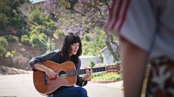 Movie still from “How It Ends” (2021), directed by Daryl Wein – A woman sitting on the ground playing a guitar; Medium shot, Low angle