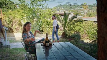 Movie still from “How It Ends” (2021), directed by Daryl Wein – A woman sitting at a table with a bottle of wine; Wide shot, High angle