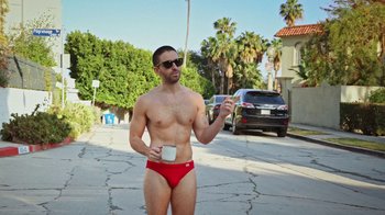Movie still from “How It Ends” (2021), directed by Daryl Wein – A man in a red swim suit is holding a cup; Wide shot, Low angle