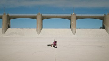 Movie still from “How It Ends” (2021), directed by Daryl Wein – A man kneeling down on the ground in front of a bridge; Extreme Wide shot, Low angle