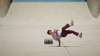 Movie still from “How It Ends” (2021), directed by Daryl Wein – A man doing a hand stand with a boombox laying on the ground behind him; Wide shot, Low angle