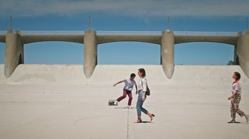 Movie still from “How It Ends” (2021), directed by Daryl Wein – Two young people are skateboarding in an open area; Wide shot, Low angle