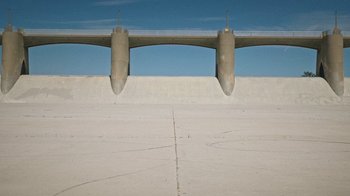 Movie still from “How It Ends” (2021), directed by Daryl Wein – A large concrete wall with a bridge in the background; Extreme Wide shot, High angle