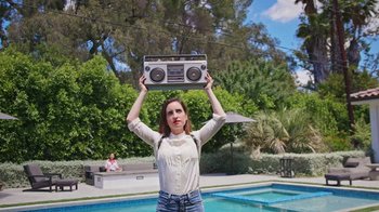 Movie still from “How It Ends” (2021), directed by Daryl Wein – A woman holding up an old fashioned boombox over her head in front of a swimming pool; Medium shot, Low angle