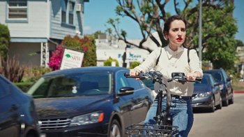 Movie still from “How It Ends” (2021), directed by Daryl Wein – A woman riding a bike down a street with cars behind it; Medium shot, Over the shoulder angle