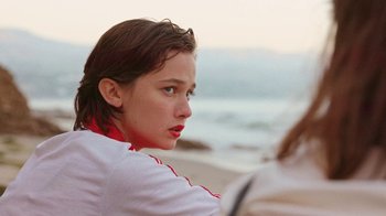 Movie still from “How It Ends” (2021), directed by Daryl Wein – A young girl is sitting on the beach looking into the distance; Close Up shot, Over the shoulder angle