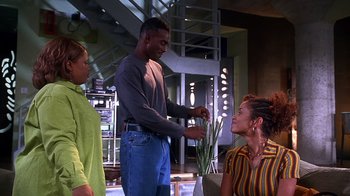 Movie still from “How to Be a Player” (1997), directed by Lionel C. Martin – A man standing next to two women in front of a potted plant; Medium shot, High angle