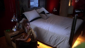 Movie still from “How to Be a Player” (1997), directed by Lionel C. Martin – A woman sitting on a chair in front of a bed; Wide shot, High angle