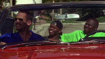 Movie still from “How to Be a Player” (1997), directed by Lionel C. Martin – Two men in a red car smiling for the camera; Medium shot, Over the shoulder angle