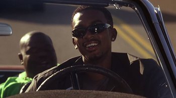 Movie still from “How to Be a Player” (1997), directed by Lionel C. Martin – A man driving a car wearing sunglasses and a jacket; Close Up shot, Low angle