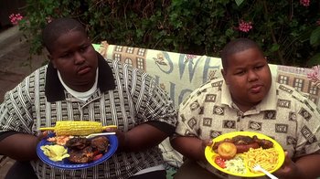 Movie still from “How to Be a Player” (1997), directed by Lionel C. Martin – A couple of men sitting next to each other holding plates of food; Medium shot, Low angle