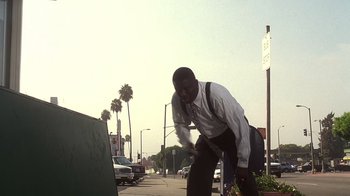 Movie still from “How to Be a Player” (1997), directed by Lionel C. Martin – A man in a white dress shirt and blue pants riding a skate board; Wide shot, Low angle