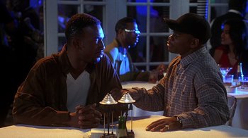 Movie still from “How to Be a Player” (1997), directed by Lionel C. Martin – A couple of men sitting next to each other at a table; Medium shot, Over the shoulder angle