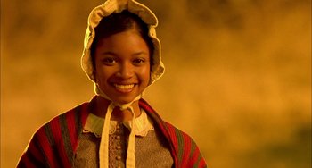 Movie still from “How to Make an American Quilt” (1995), directed by Jocelyn Moorhouse – A young woman wearing an apron and a bonnet smiles; Close Up shot, Low angle