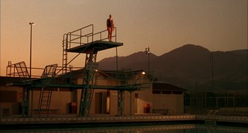 Movie still from “How to Make an American Quilt” (1995), directed by Jocelyn Moorhouse – A man standing on a diving platform in front of mountains; Extreme Wide shot, Low angle