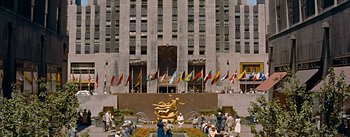 Movie still from “How to Marry a Millionaire” (1953), directed by Jean Negulesco – A group of people standing around a building with a fountain; Extreme Wide shot, High angle