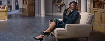 Movie still from “How to Marry a Millionaire” (1953), directed by Jean Negulesco – A woman sitting on a couch talking on a phone; Wide shot, Low angle