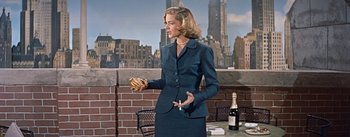 Movie still from “How to Marry a Millionaire” (1953), directed by Jean Negulesco – A woman standing on a balcony holding a cigarette and wearing a suit; Medium shot, Low angle