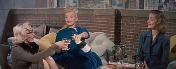 Movie still from “How to Marry a Millionaire” (1953), directed by Jean Negulesco – A woman sitting on a couch holding a glass of wine; Medium shot, High angle
