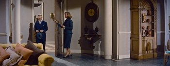 Movie still from “How to Marry a Millionaire” (1953), directed by Jean Negulesco – A woman in a blue suit is standing in front of a clock; Wide shot, Low angle