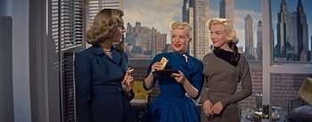 Movie still from “How to Marry a Millionaire” (1953), directed by Jean Negulesco – A group of women standing next to each other holding a piece of cake; Medium shot, Low angle