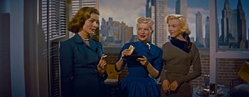 Movie still from “How to Marry a Millionaire” (1953), directed by Jean Negulesco – A group of women standing next to each other holding sandwiches; Medium shot, Low angle