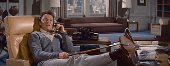 Movie still from “How to Marry a Millionaire” (1953), directed by Jean Negulesco – A man sitting on a couch talking on the phone; Medium shot, High angle