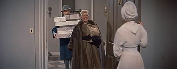 Movie still from “How to Marry a Millionaire” (1953), directed by Jean Negulesco – An older woman in a fur coat carrying a stack of boxes; Medium shot, Over the shoulder angle
