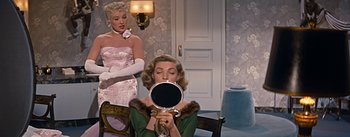 Movie still from “How to Marry a Millionaire” (1953), directed by Jean Negulesco – A woman in a green dress holding up a mirror in front of another woman in a pink dress; Medium shot, Over the shoulder angle