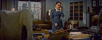 Movie still from “How to Marry a Millionaire” (1953), directed by Jean Negulesco – A woman talking on a phone while a man plays a guitar; Wide shot, High angle