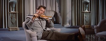Movie still from “How to Marry a Millionaire” (1953), directed by Jean Negulesco – A man sitting on a couch holding a wooden stick; Medium shot, Low angle