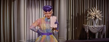 Movie still from “How to Marry a Millionaire” (1953), directed by Jean Negulesco – A woman in a colorful dress holding a pink envelope; Medium shot, Low angle