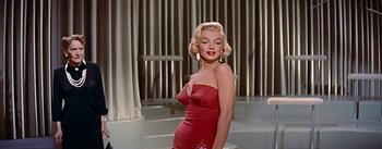 Movie still from “How to Marry a Millionaire” (1953), directed by Jean Negulesco – A woman in a red dress posing for a picture; Medium shot, Low angle
