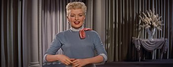 Movie still from “How to Marry a Millionaire” (1953), directed by Jean Negulesco – A woman with blonde hair wearing a blue shirt and a pink neck tie; Medium shot, Low angle