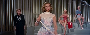 Movie still from “How to Marry a Millionaire” (1953), directed by Jean Negulesco – A beautiful woman in a dress holding a white cane; Medium shot, Low angle