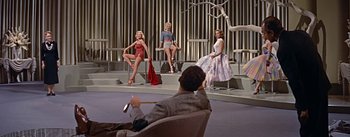 Movie still from “How to Marry a Millionaire” (1953), directed by Jean Negulesco – A man sitting in front of three women in dresses; Wide shot, Low angle