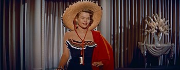 Movie still from “How to Marry a Millionaire” (1953), directed by Jean Negulesco – A woman wearing a straw hat and holding a red shawl; Medium shot, Low angle