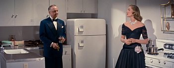 Movie still from “How to Marry a Millionaire” (1953), directed by Jean Negulesco – A man and a woman standing next to a white refrigerator; Medium shot, Over the shoulder angle