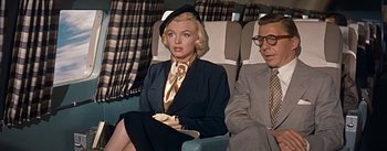 Movie still from “How to Marry a Millionaire” (1953), directed by Jean Negulesco – A woman sitting on top of an airplane next to an older man; Medium shot, Low angle
