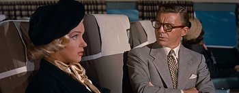 Movie still from “How to Marry a Millionaire” (1953), directed by Jean Negulesco – A man and a woman sitting next to each other on a plane; Close Up shot, Over the shoulder angle