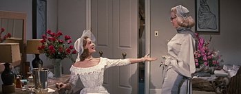 Movie still from “How to Marry a Millionaire” (1953), directed by Jean Negulesco – A woman wearing a white dress and a hat; Medium shot, Over the shoulder angle