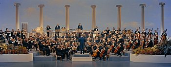 Movie still from “How to Marry a Millionaire” (1953), directed by Jean Negulesco – A group of men in black suits and black hats are sitting in front of a conductor; Extreme Wide shot, Low angle